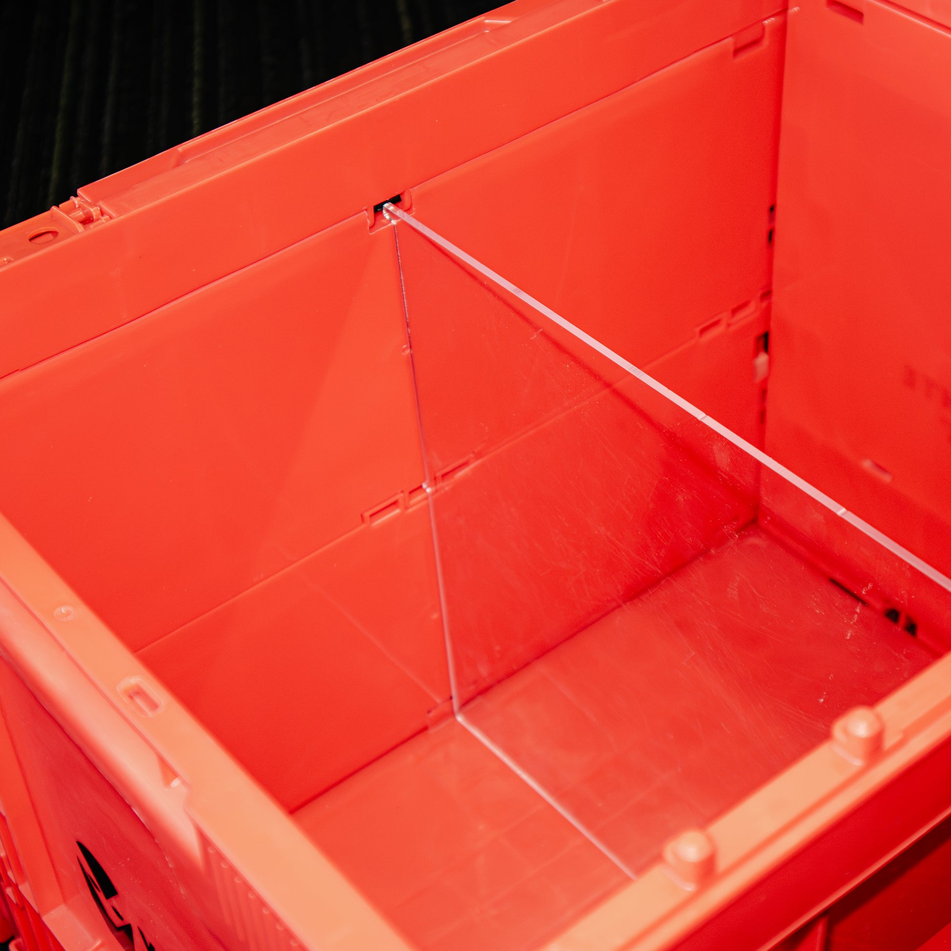 Close-up of a bright orange-red plastic storage bin or crate interior with a clear divider panel and a white cord running across the compartment.