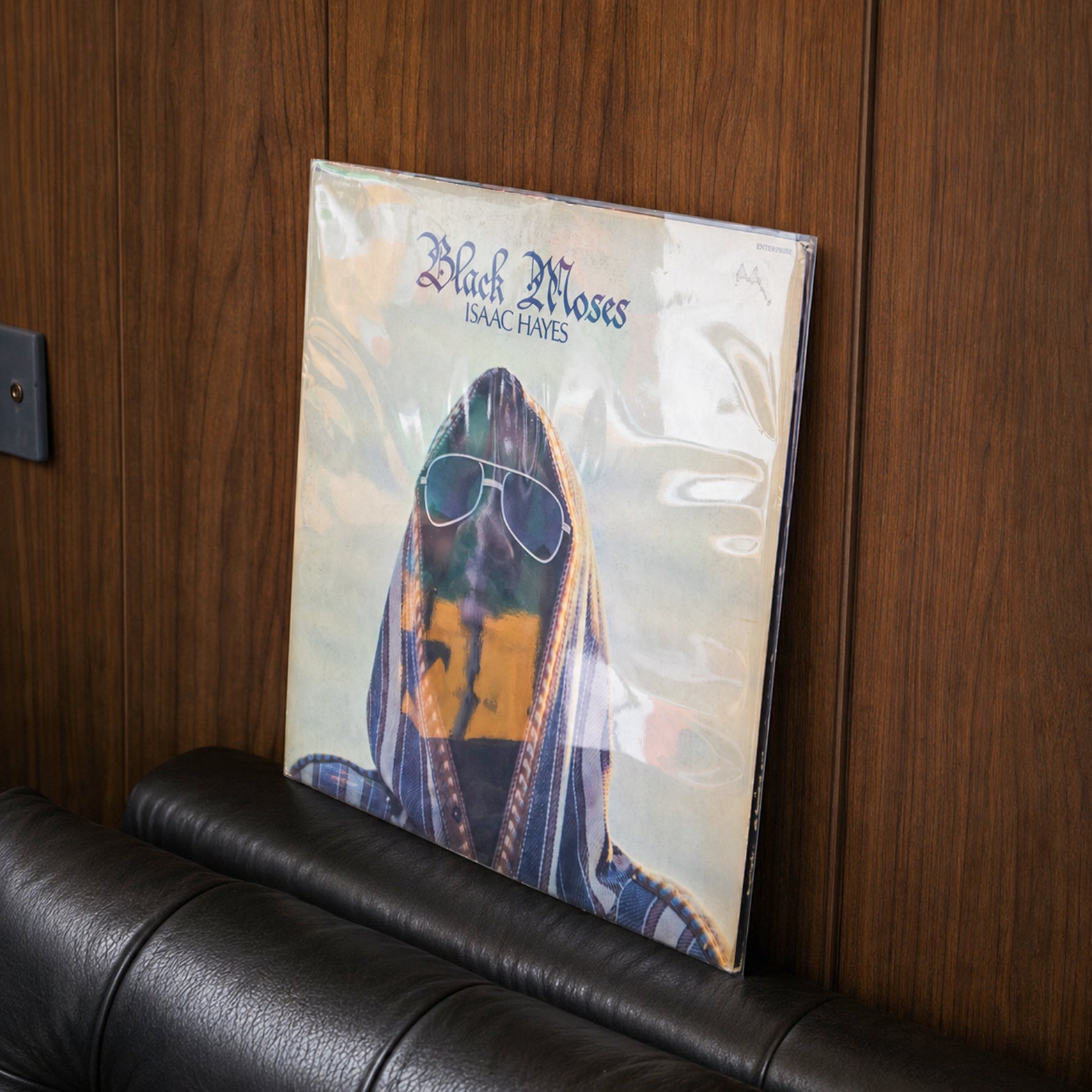 A vinyl record album for Black Moses / Isolationist, resting on a black leather couch against a dark wood-paneled wall.